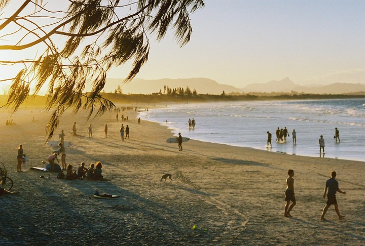 A beach is filled with people and a dog at sunset, with mountains in the distance.