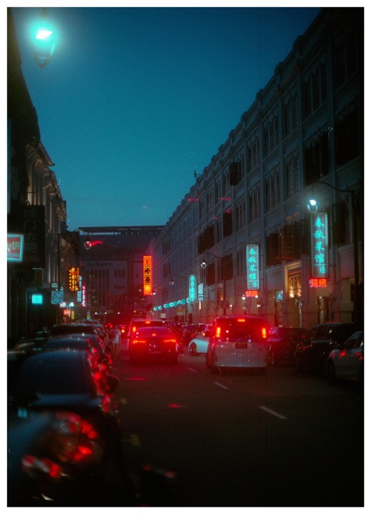 A street is filled with cars and neon signs at night in Chinatown.