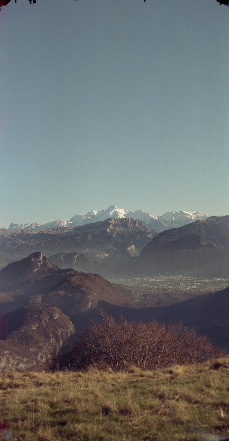 A vast mountain landscape shows snow-capped peaks in the distance, with a valley and town visible below.
