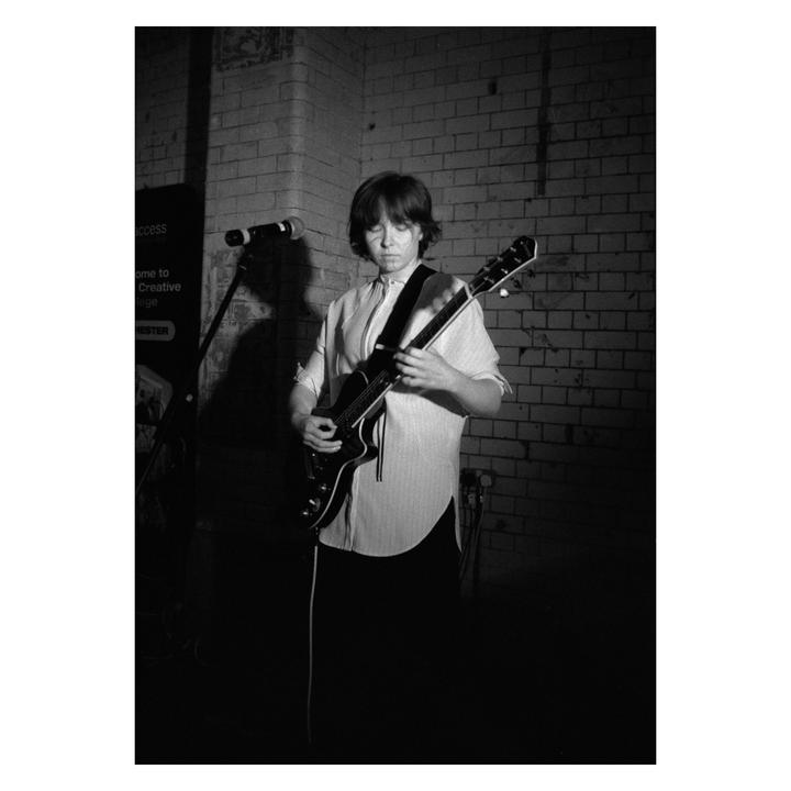 A woman plays an electric guitar in front of a brick wall.