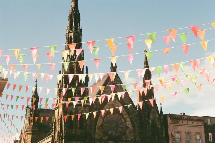 Colorful bunting hangs above a gothic church with a tall spire against a clear sky.