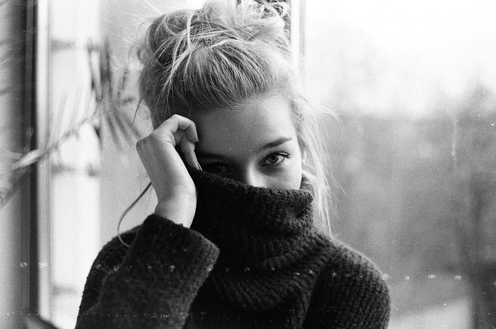 A woman with her hair in a bun pulls a turtleneck sweater up to cover her nose and mouth.