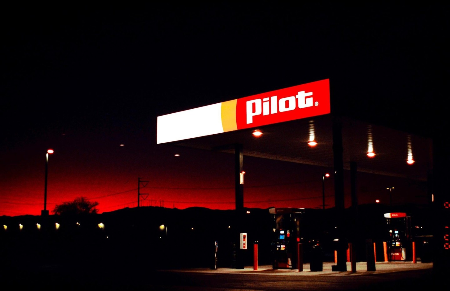 A gas station with a red and white Pilot sign is illuminated at night against a red sky.