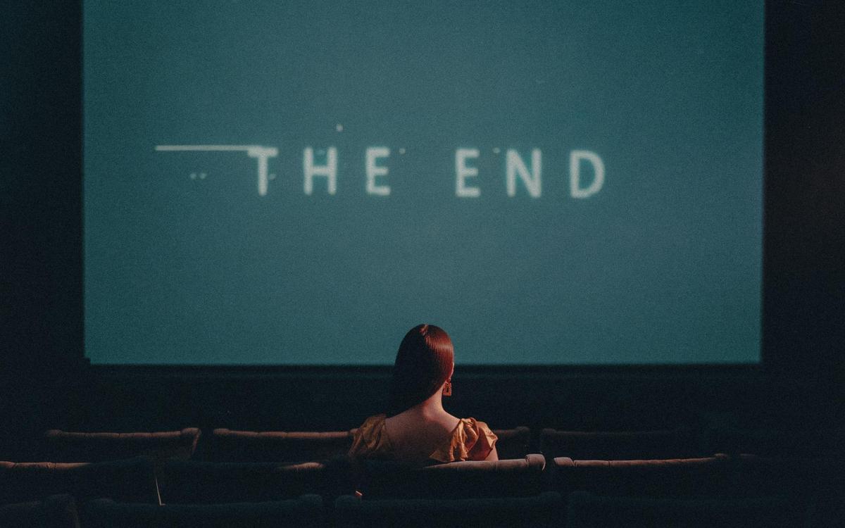 A woman with red hair sits in a movie theater watching "The End" on the screen.