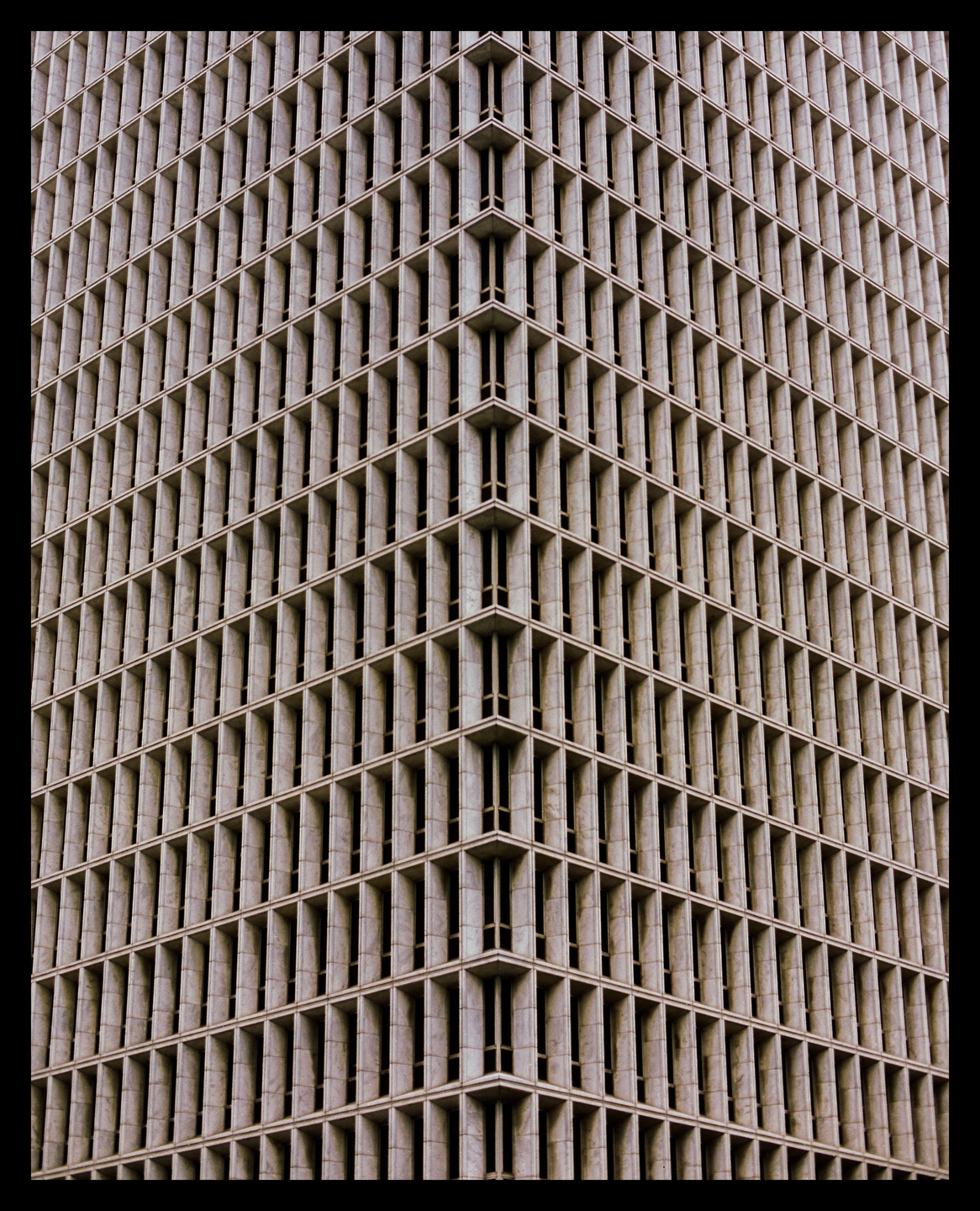 The corner of a tall building with many windows is shown from a low angle.