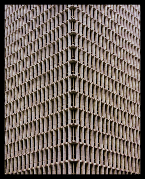 The corner of a tall building with many windows is shown from a low angle.