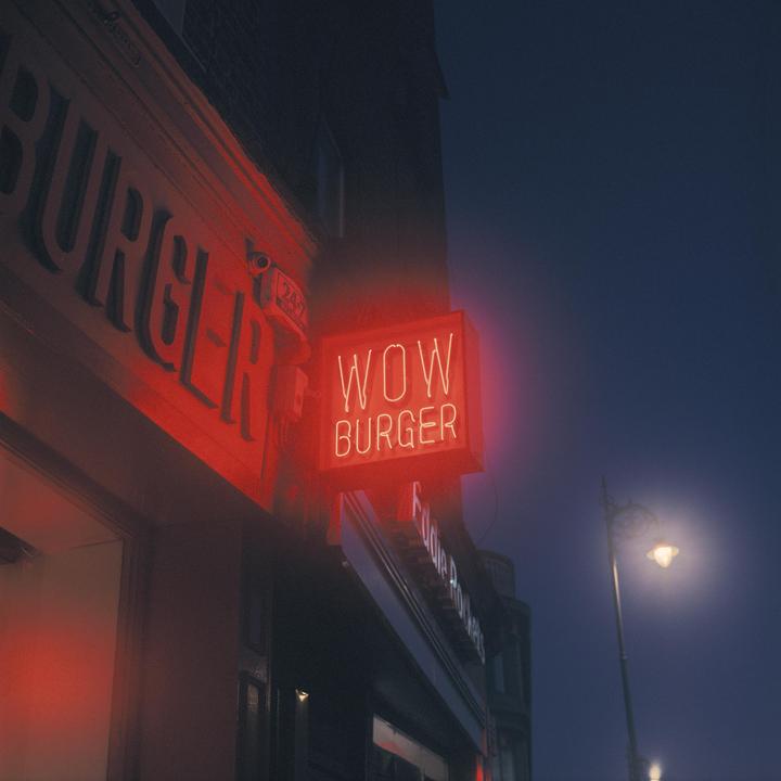 A red neon sign for "Wow Burger" is illuminated on a building at night.