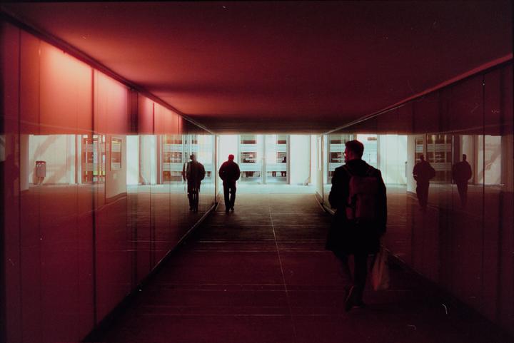 Three men walk through a red-lit tunnel with reflections on the walls.