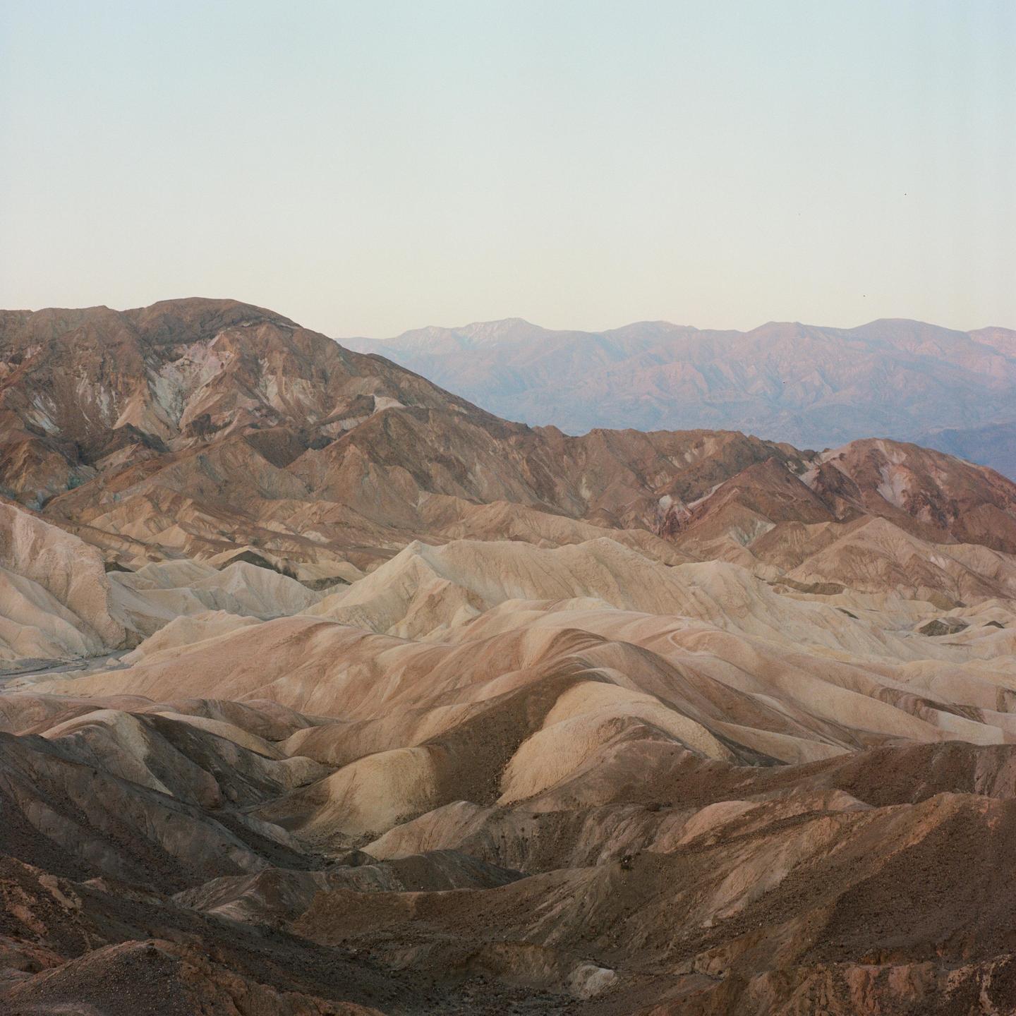 A vast desert landscape features rolling hills and mountains under a pale sky.