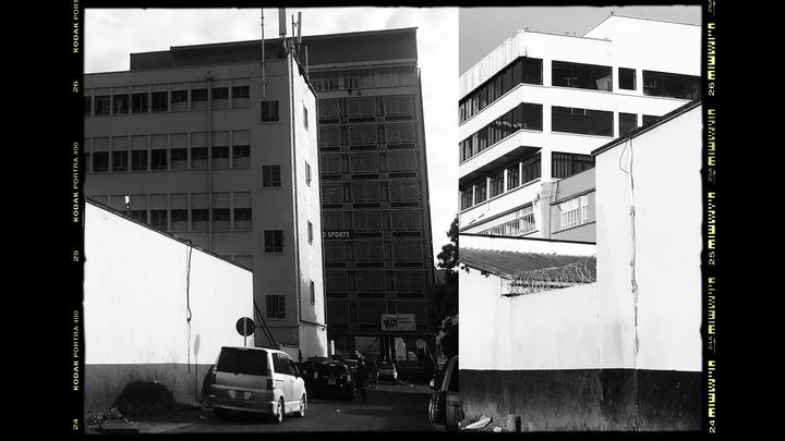 A street scene shows several buildings, a white van, and a wall with barbed wire.