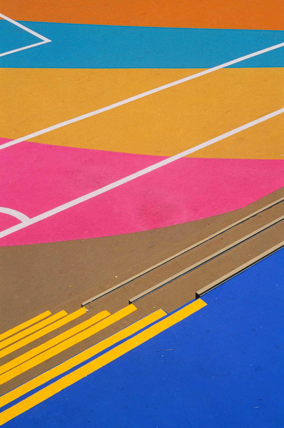 A colorful playground surface features various painted lines and shapes in orange, blue, yellow, pink, brown, and white.