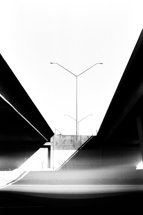 Two overpasses frame a concrete wall with streetlights and shadows.