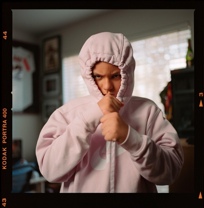 A boy in a pink hooded sweatshirt holds his fists up to his face.
