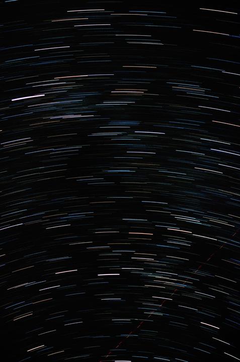 A long exposure photograph captures the movement of stars and satellites across a dark night sky.