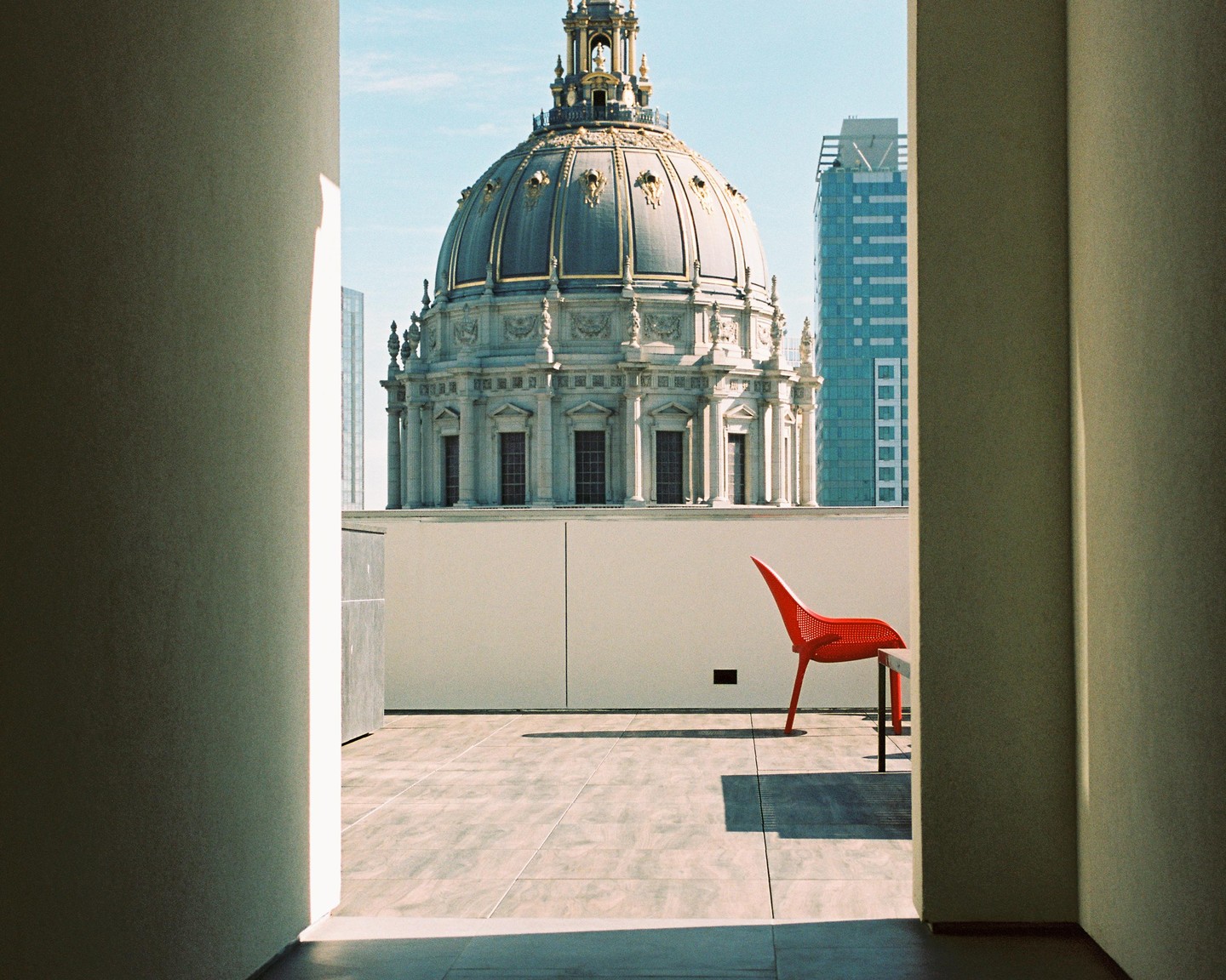 A red chair sits on a patio with a domed building and a skyscraper in the background.
