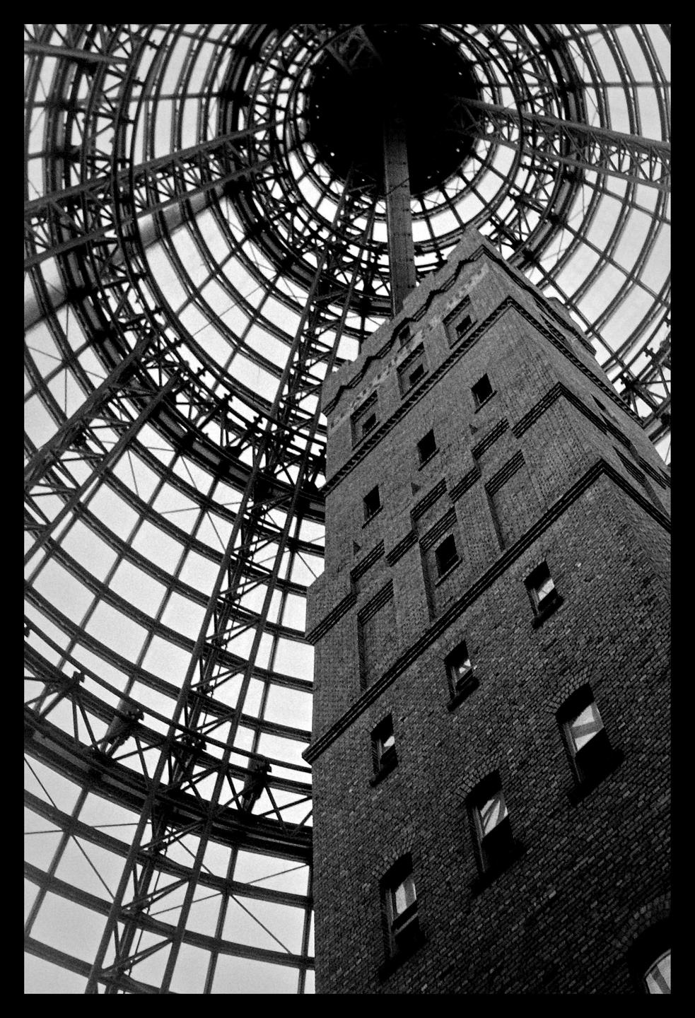 A tall brick building stands next to a large, circular, glass and metal dome structure.