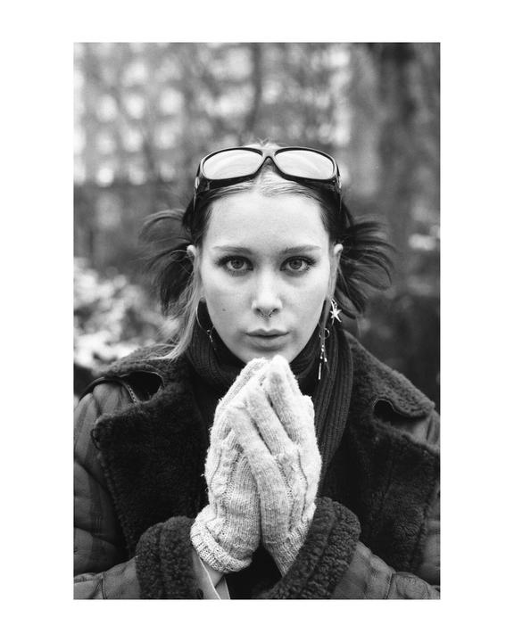A woman with sunglasses on her head and knitted gloves on her hands looks directly at the viewer.