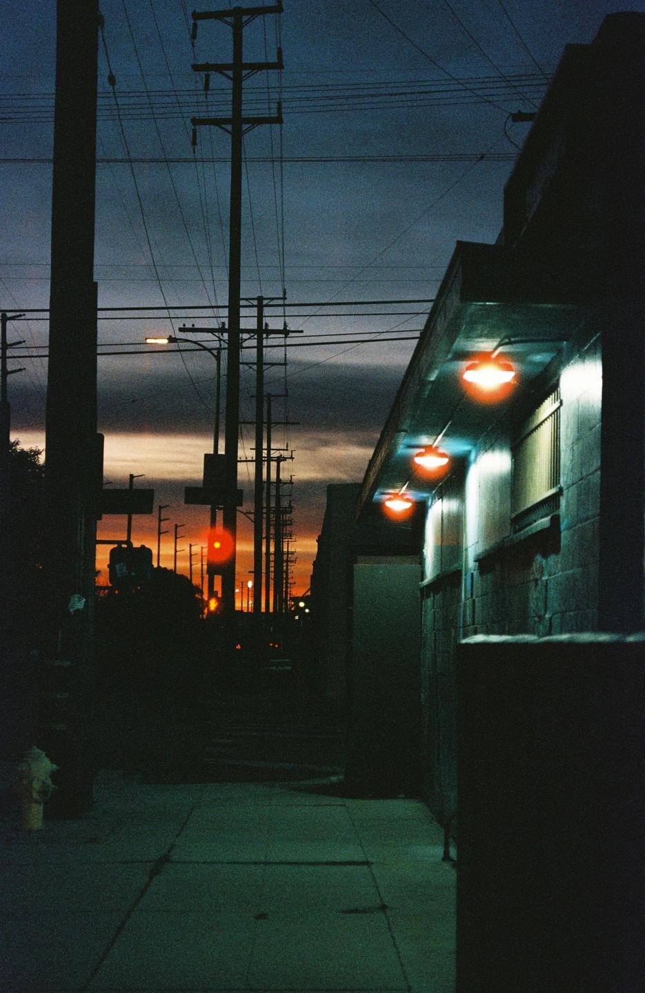 A dark street with power lines and a building with orange lights is visible at sunset.