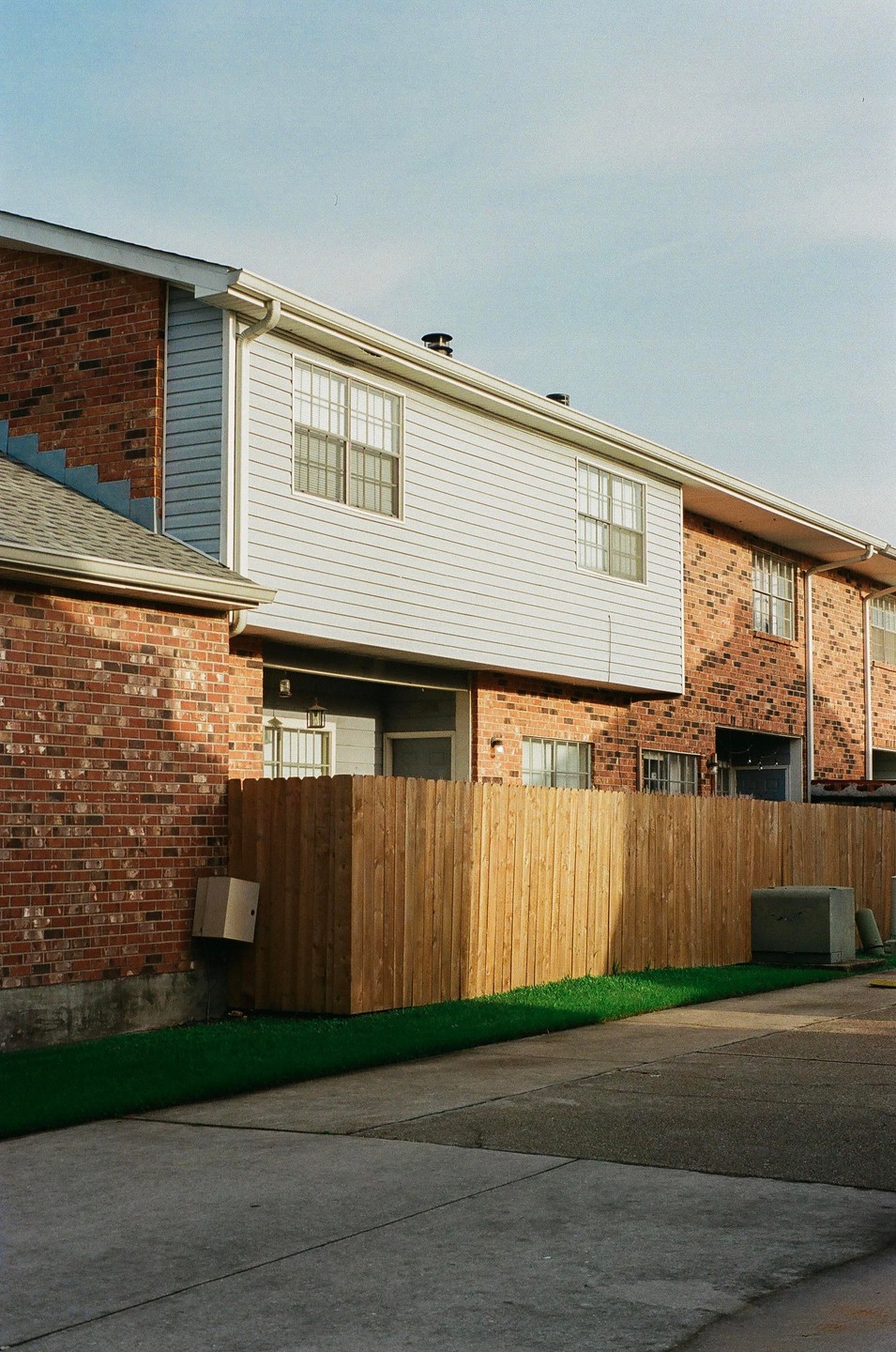 A row of brick and siding townhouses with a wooden fence and a strip of artificial grass in front.
