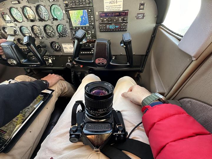 A camera rests on a person's lap in the cockpit of an airplane.