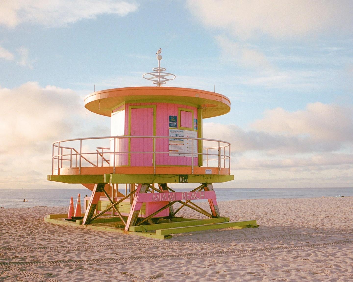 A colorful lifeguard stand sits on a sandy beach next to the ocean under a partly cloudy sky.