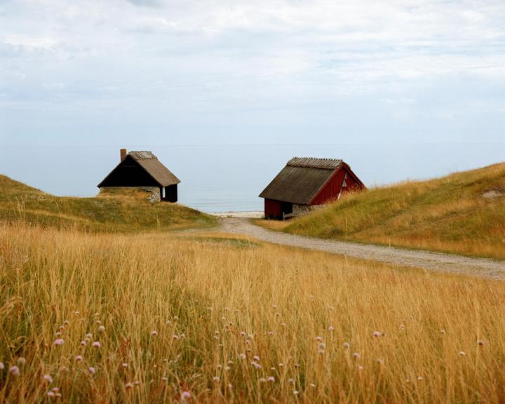 Two small sheds with thatched roofs sit on grassy hills overlooking the sea.