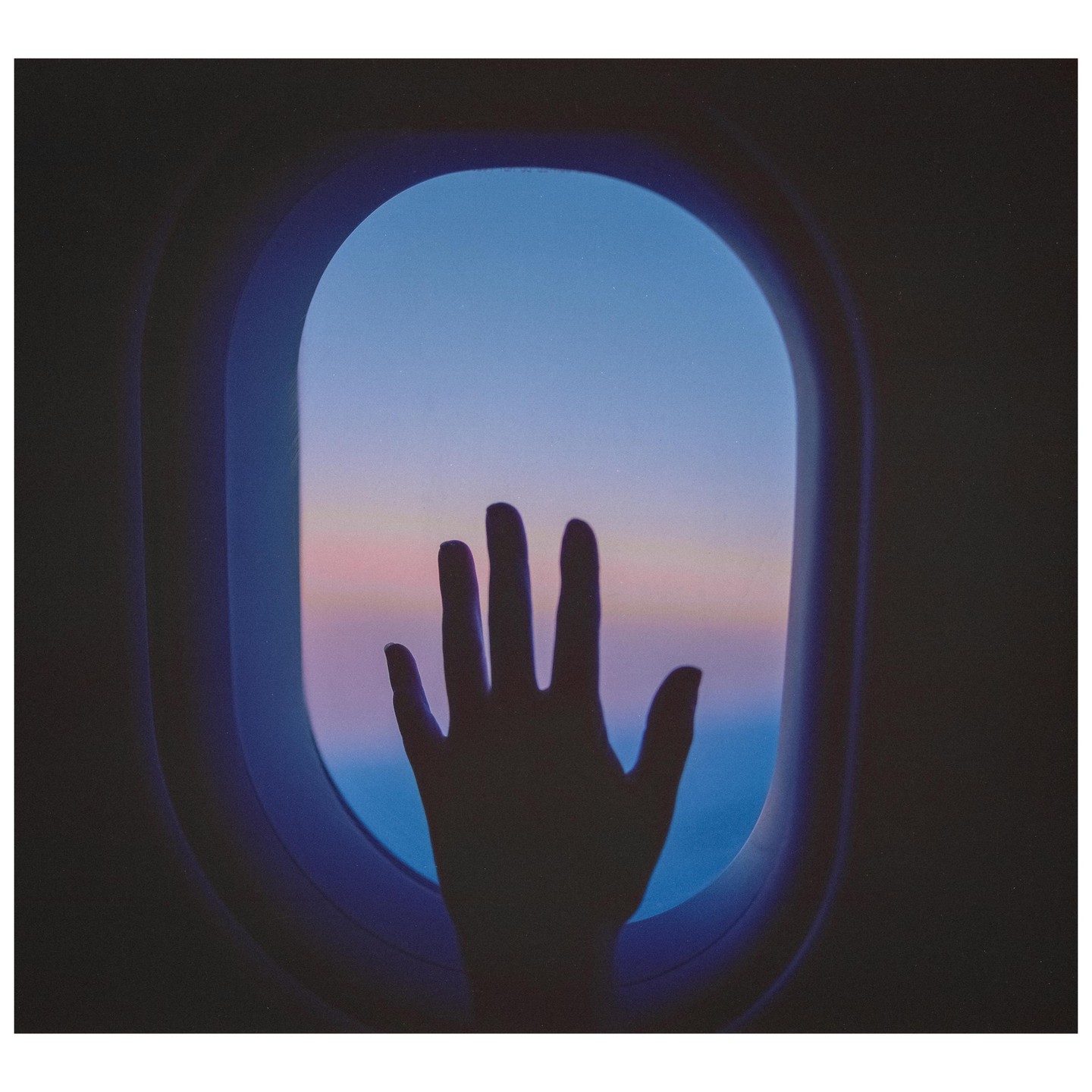 A hand is silhouetted against an airplane window with a colorful sky outside.