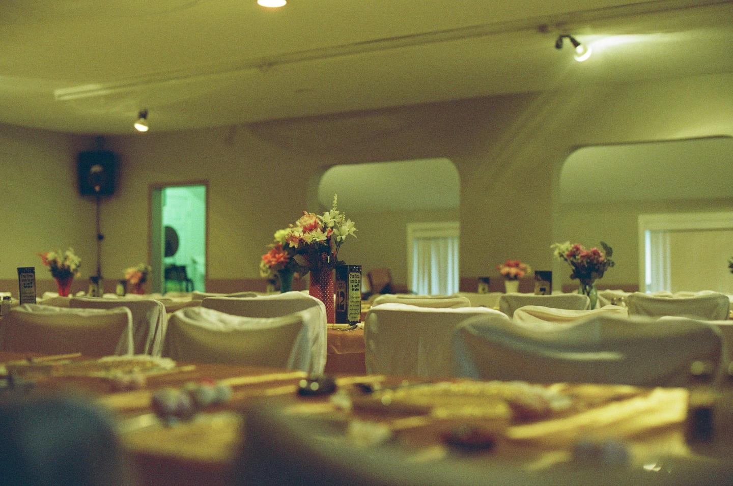 A long table is set with white chairs and flower arrangements in a room with arched doorways.