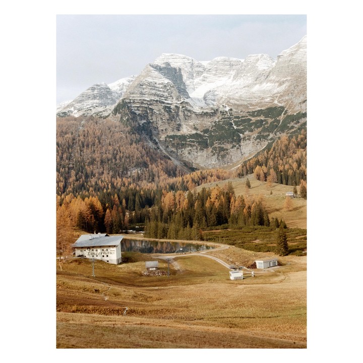 A white building with "Linzerhaus" written on it sits next to a pond, surrounded by autumn trees and snow-capped mountains.