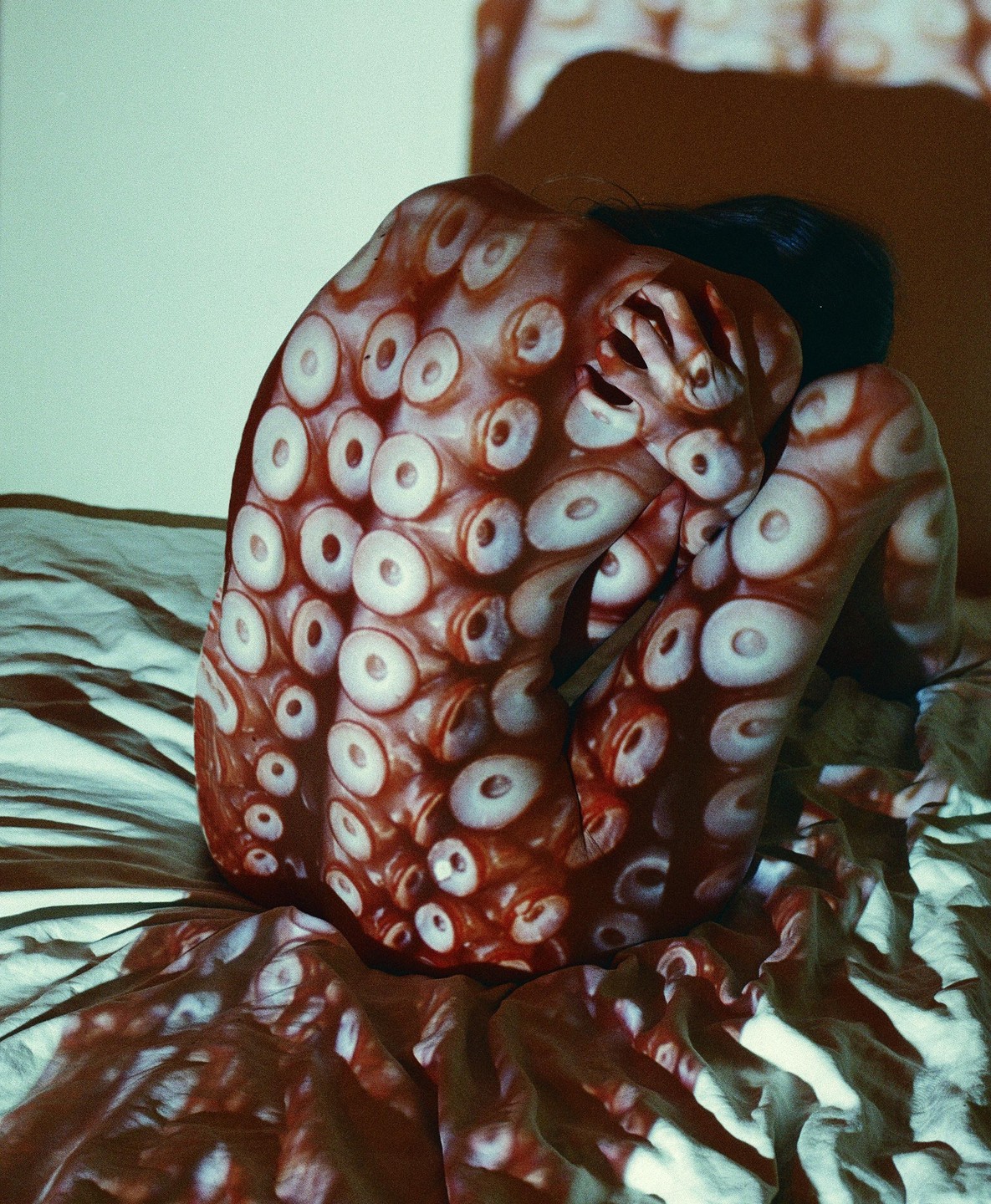 A person is curled up on a bed with an octopus tentacle pattern projected onto their body and the sheets.