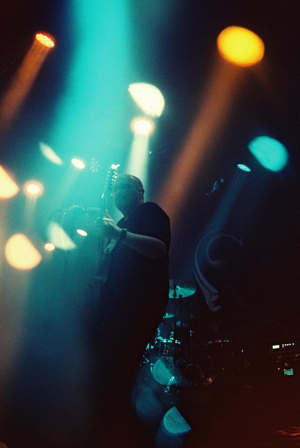 A man plays guitar on a stage illuminated by colorful spotlights.