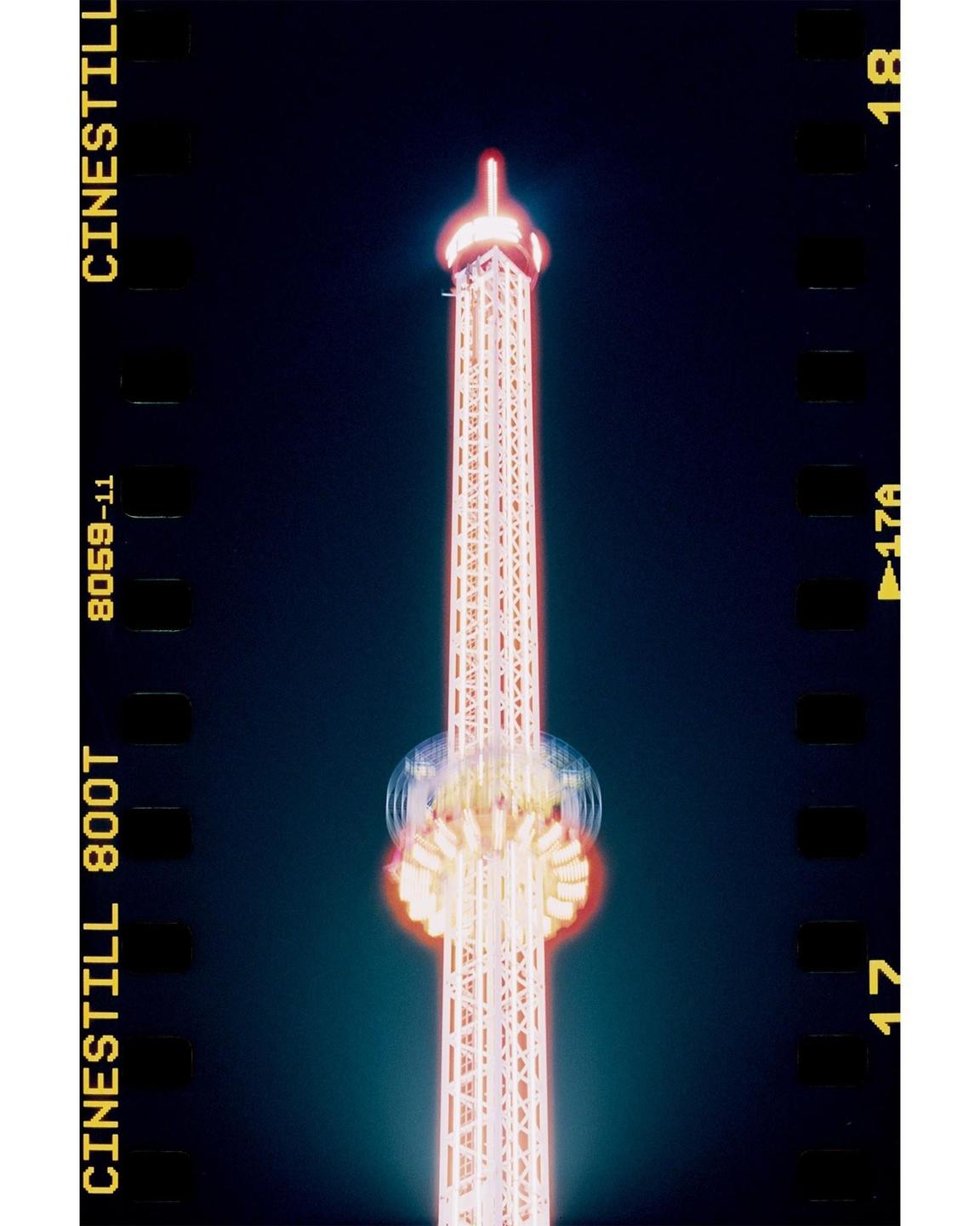 A tall amusement park ride with bright lights is captured at night against a dark sky.