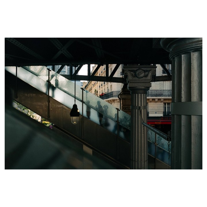 A street lamp hangs above an escalator with a building and sky visible in the background.