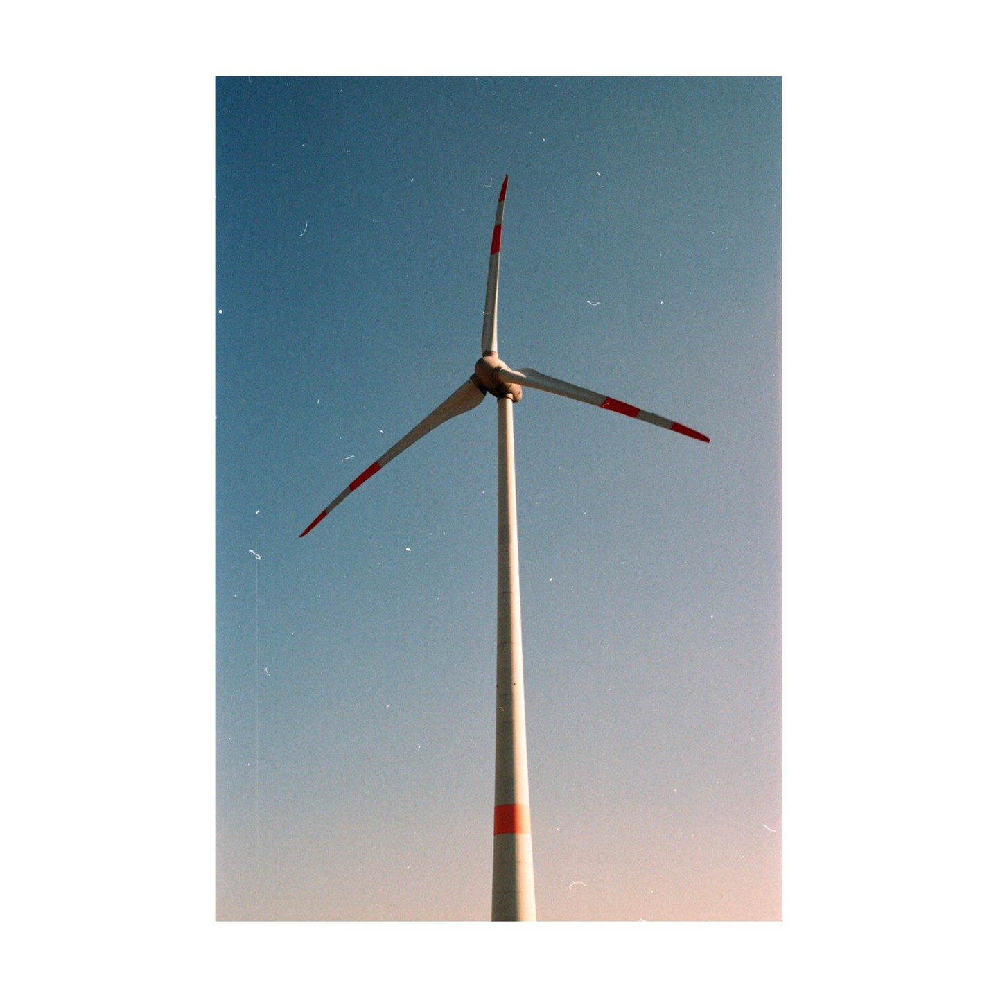 A wind turbine with red-tipped blades stands against a clear blue sky.