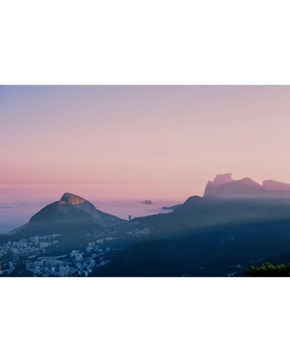 A city is nestled among mountains under a pink and purple sky at sunset.