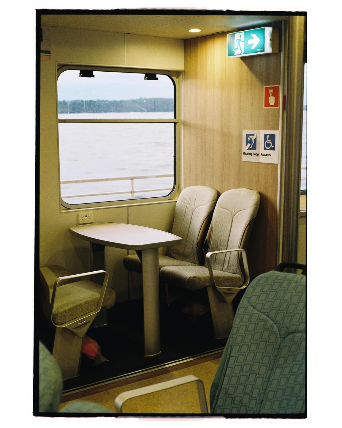 A table and chairs are visible inside a ferry cabin, with a window looking out onto the water.