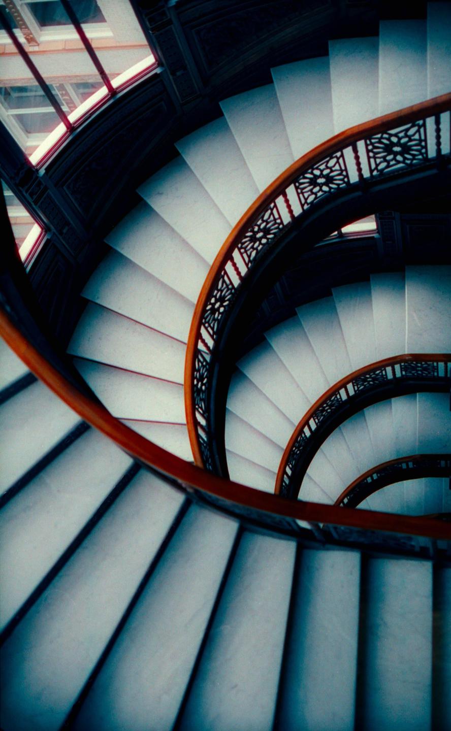A spiral staircase with a wooden handrail and ornate metalwork descends from above.