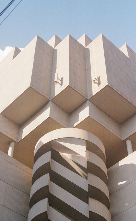 A brutalist building with a striped cylindrical structure is viewed from below against a clear sky.