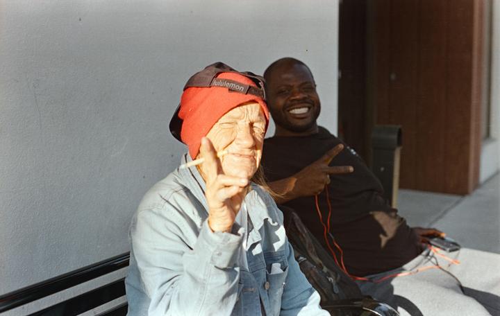 A woman in a red hat holds a cigarette and makes a peace sign next to a smiling man.