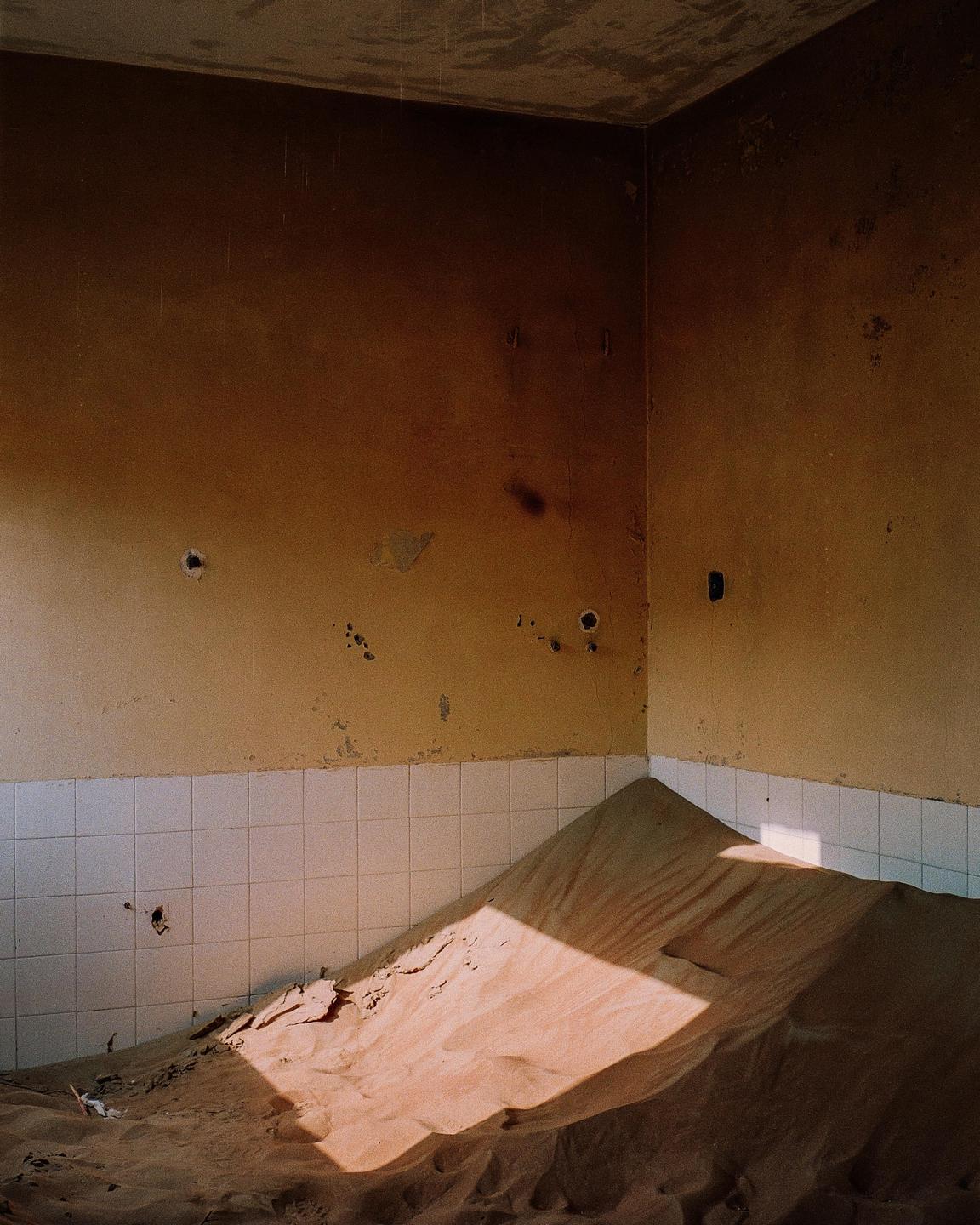 A room with sand piled high against two walls, with light shining through a window.