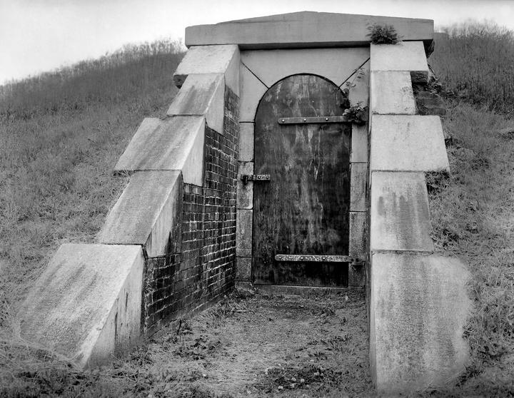 A wooden door with an arched top is set into a stone and brick structure on a grassy hillside.