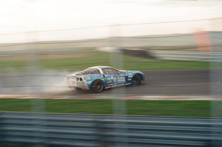 A blue and white race car drifts on a track, leaving a trail of smoke behind it.