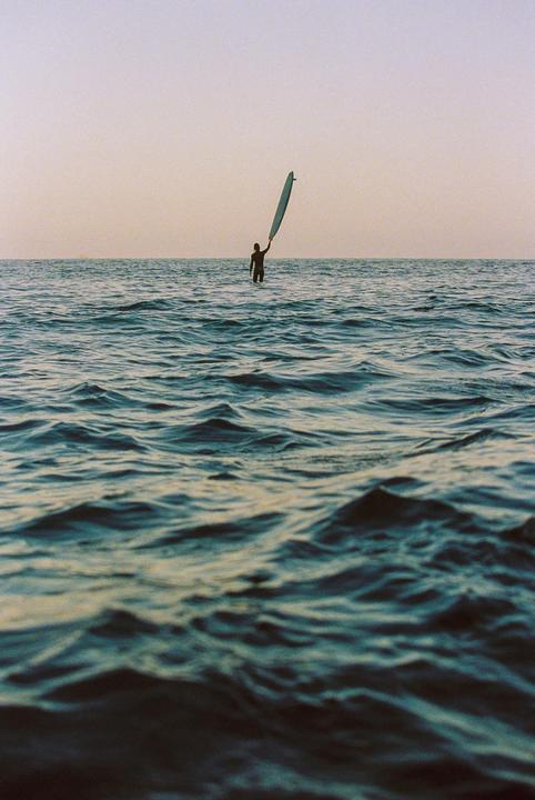 A surfer stands in the ocean holding a surfboard above their head.