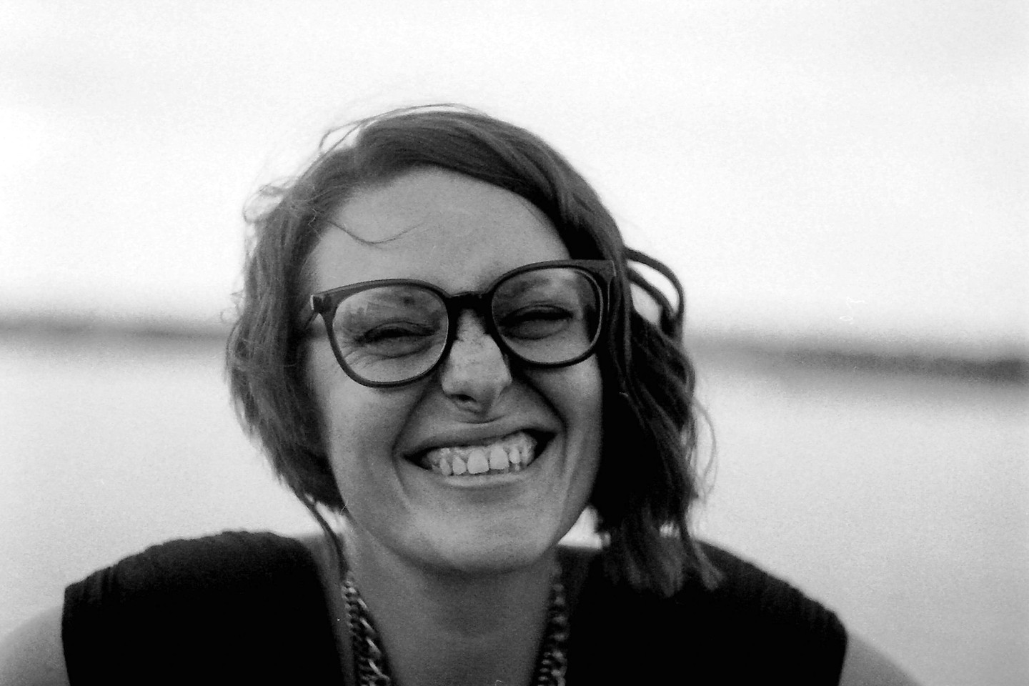 A woman with glasses smiles with her eyes closed.