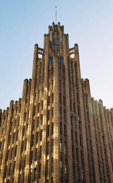 A tall, ornate building with many windows and a spire on top stands against a clear sky.