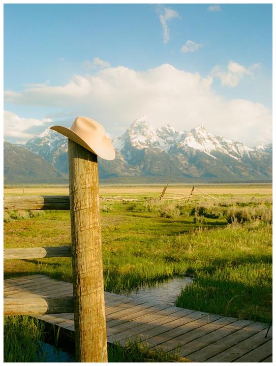 A cowboy hat rests on a wooden post with a mountain range in the background.