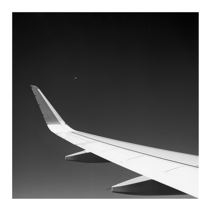 An airplane wing is visible against a dark sky with a crescent moon.