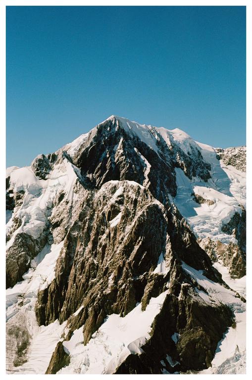 A snow-capped mountain peak rises against a clear blue sky.