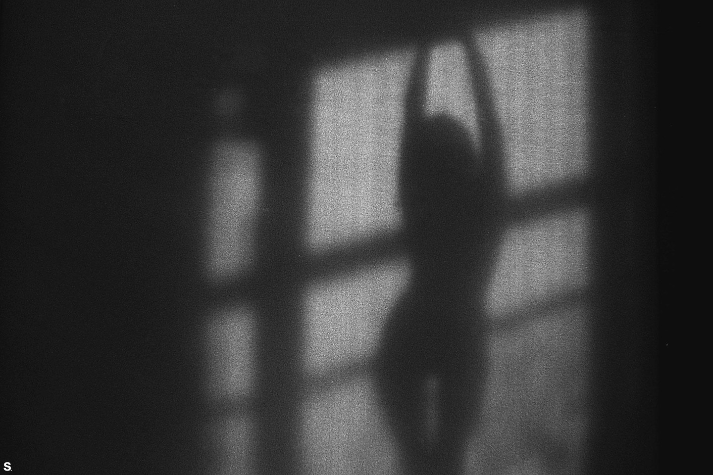 A shadow of a woman with her arms raised is cast on a wall with window pane shadows.