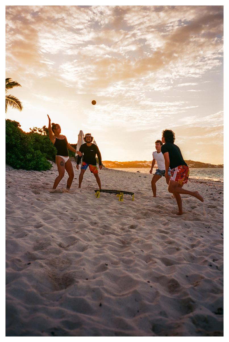 Four people play spikeball on a sandy beach at sunset.